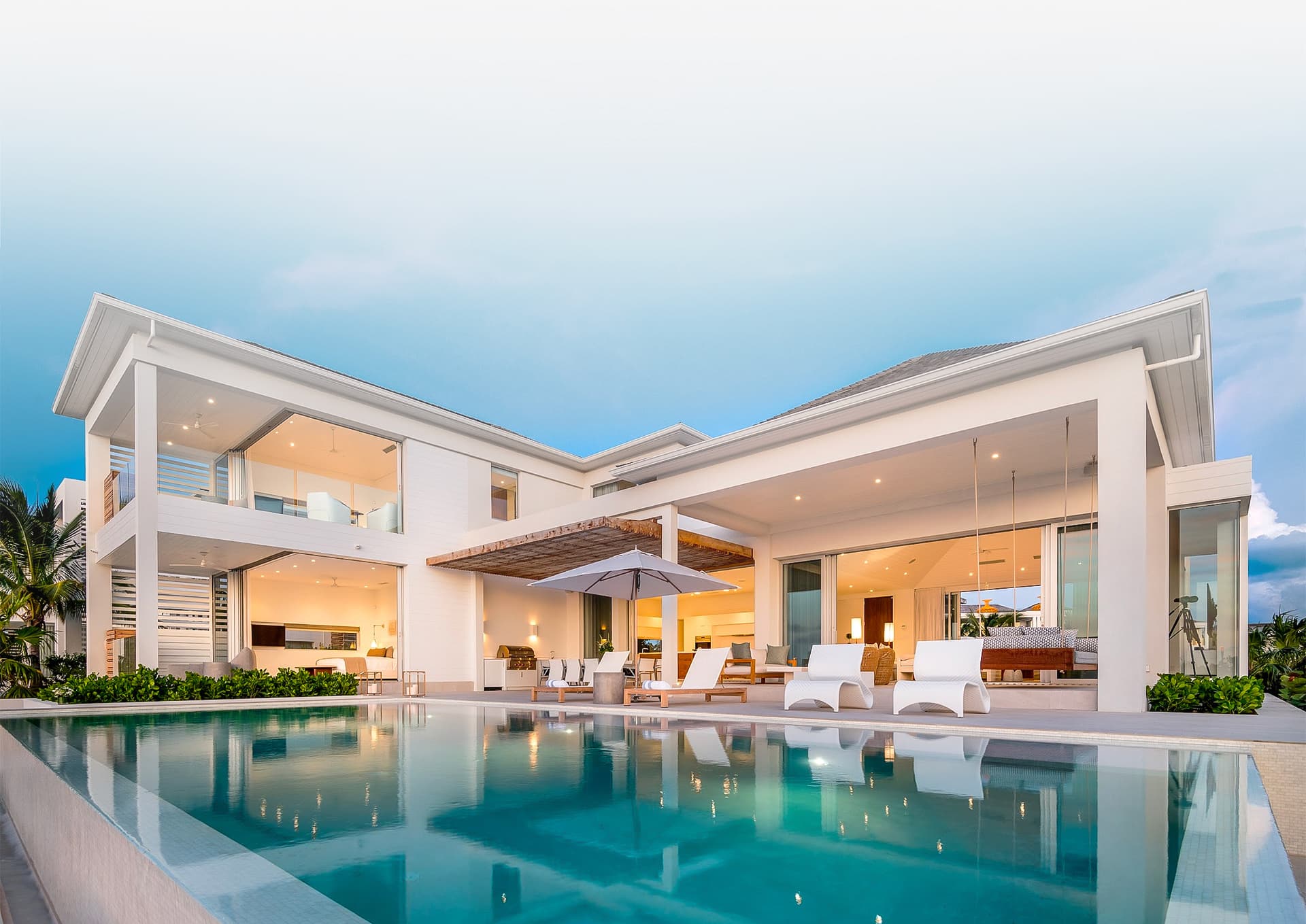 A Beach Enclave villa at twilight, its pool reflecting the lit interior